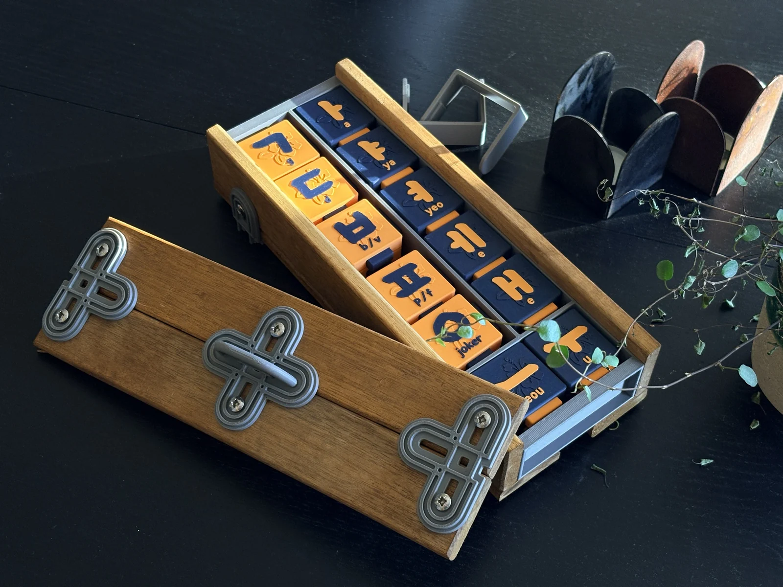 An open wooden box holding orange and blue tiles with Korean letters
