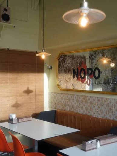 Inside Nopo 1988: white tables, orange chairs and the logo on a mirror