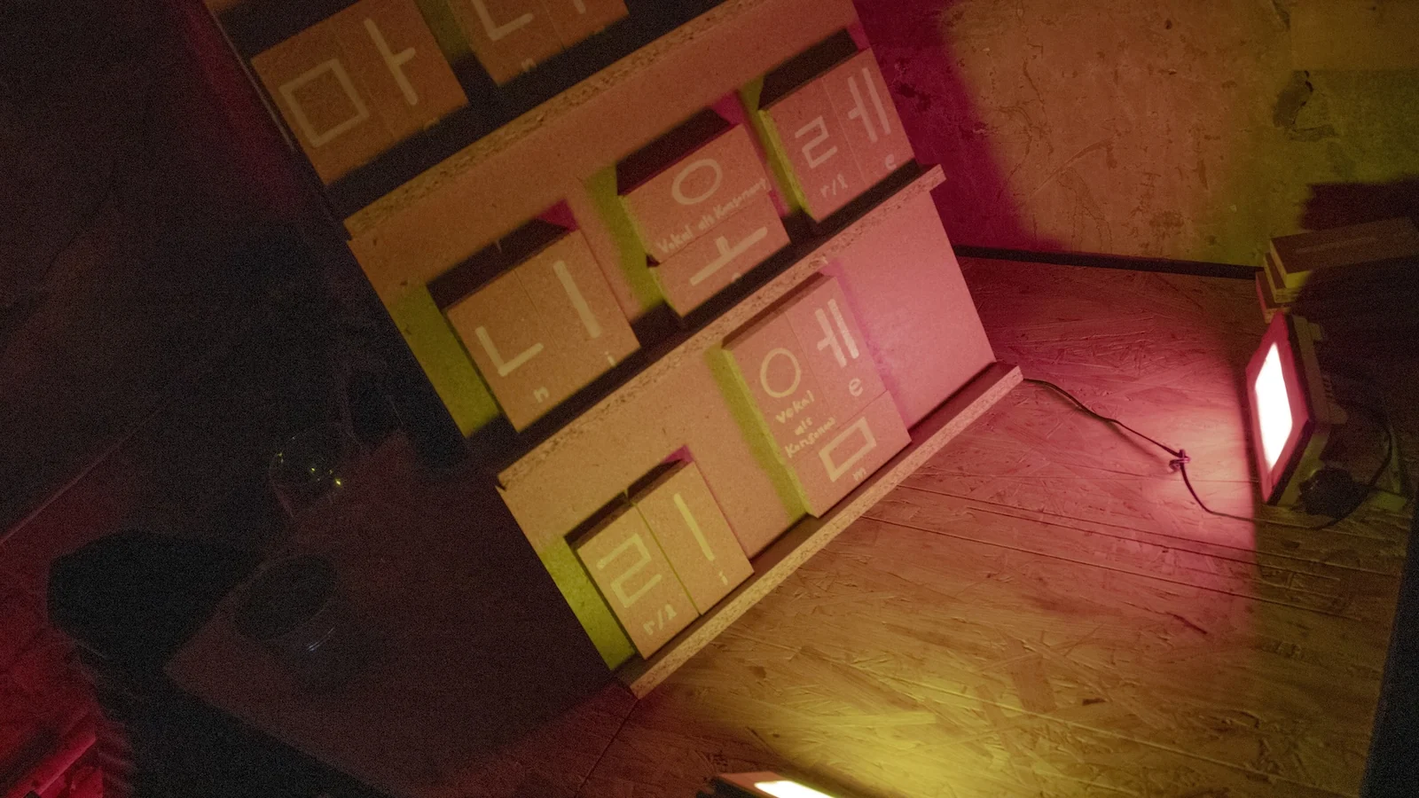 A shelf holding Korean syllables built from blocks, lit in pink and yellow